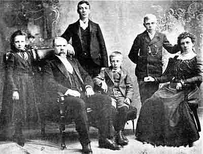 Formal family photo in Sunday best; leather chairs; youngest son in short pants and button boots.